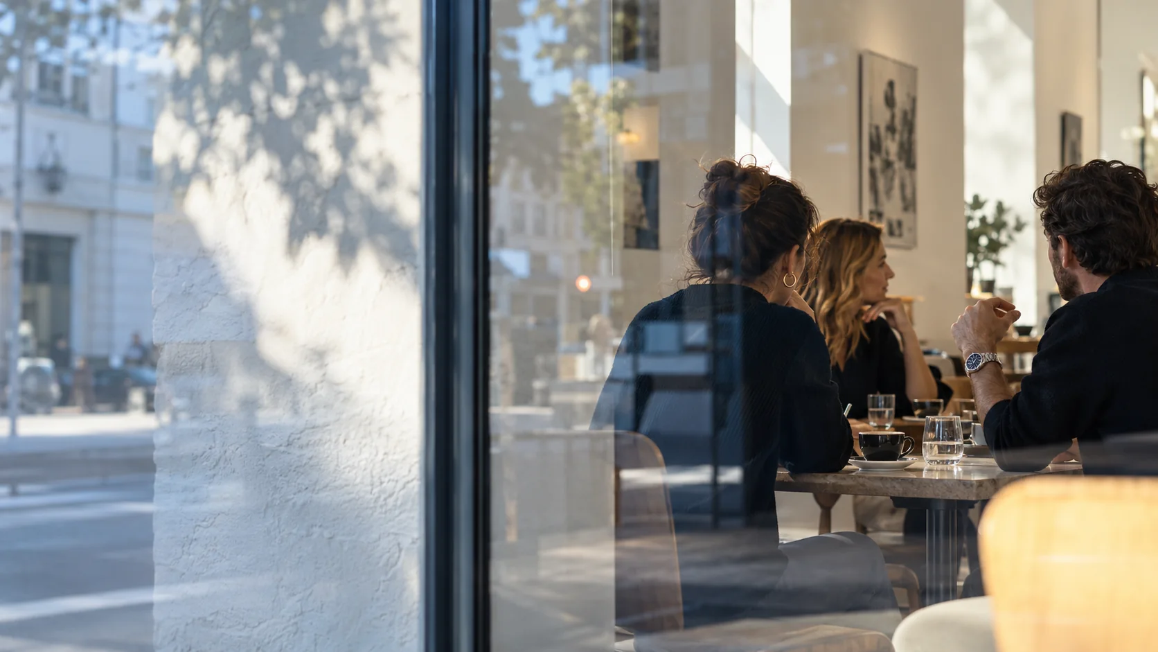 A small gathering seen through cafe glass, street reflections crossing a conversation