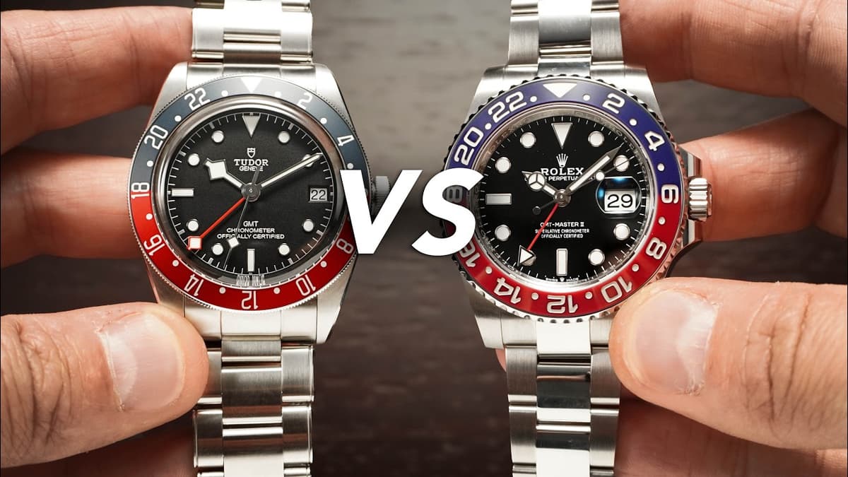 Two steel GMT wristwatches are held side by side with a large “VS” between them.