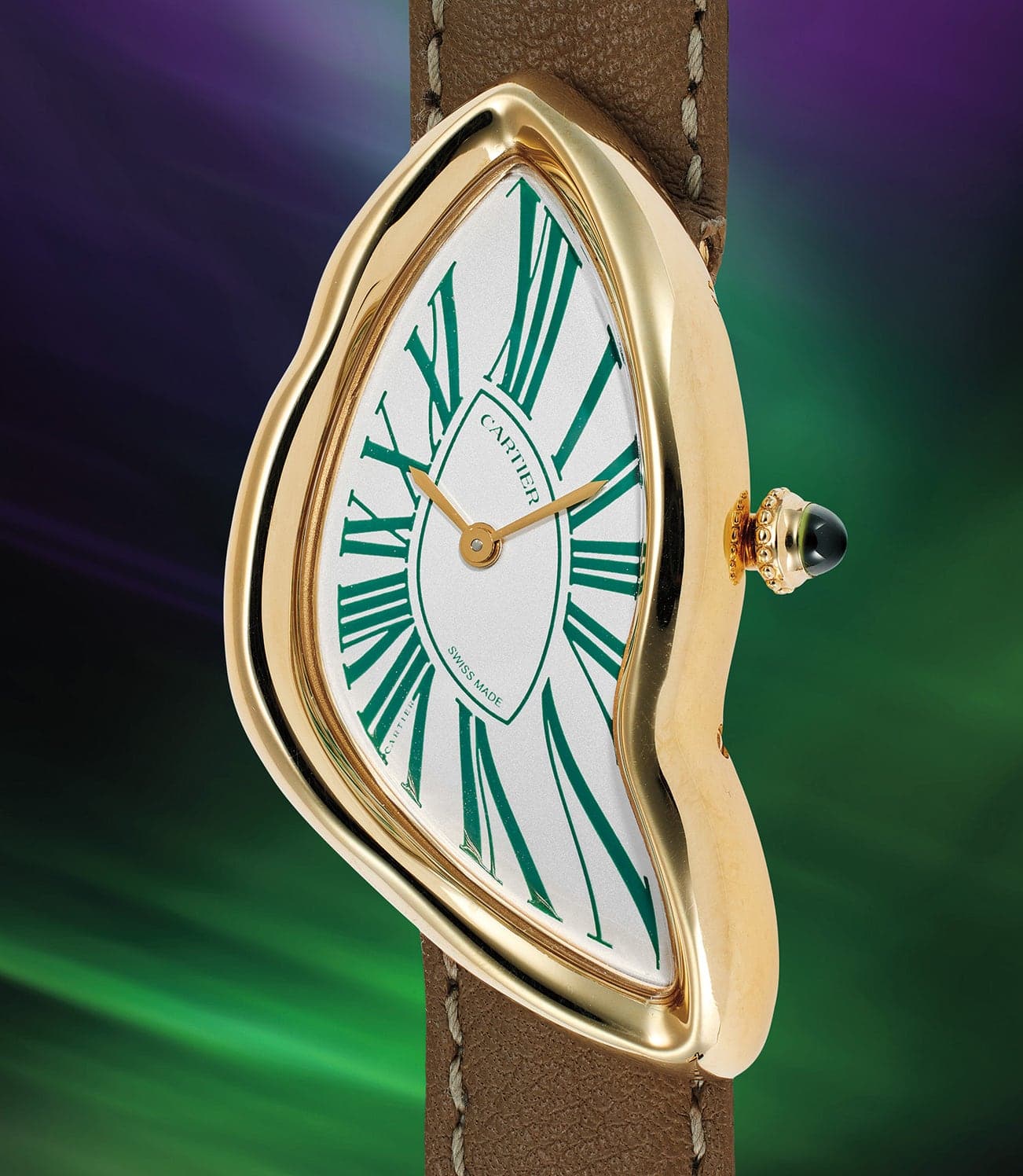 A gold, asymmetrical wristwatch with a white dial, green Roman numerals, and a brown strap on a colorful background.