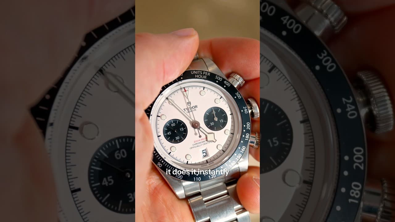 A hand holds a stainless steel chronograph watch with a white dial and black subdials.