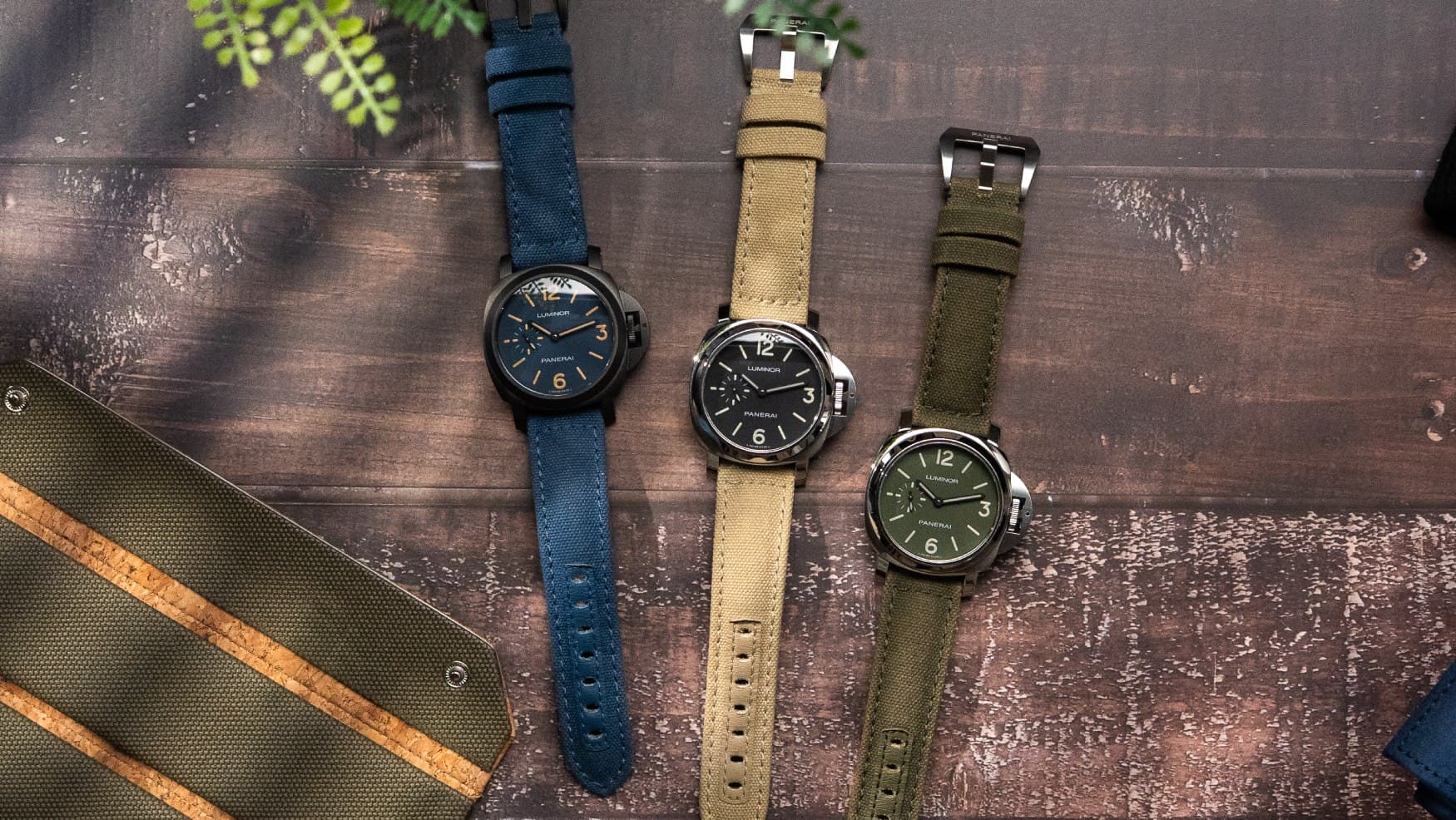 Three wristwatches with large cases and long straps arranged on a wooden surface, with one blue, one tan, and one olive dial.